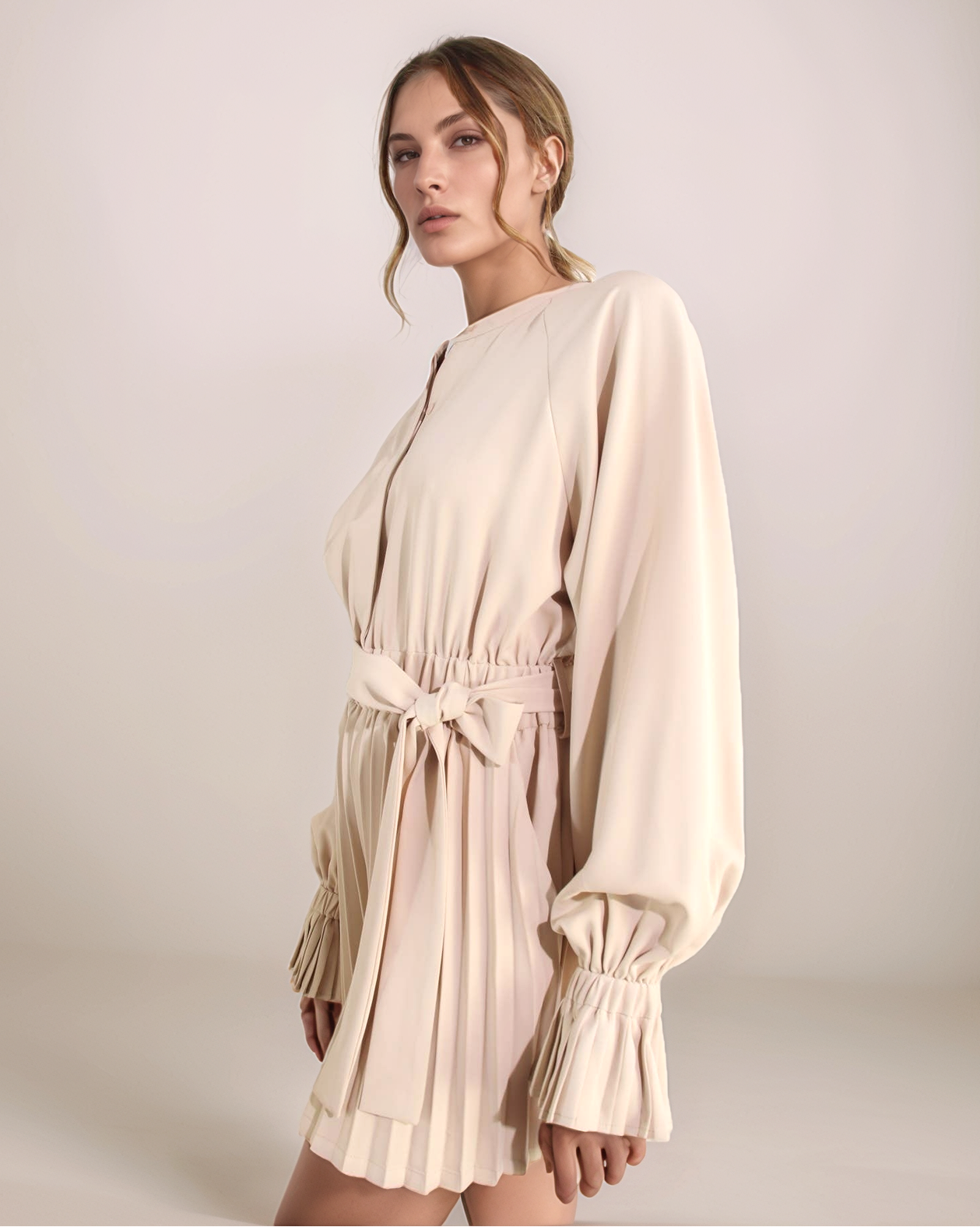 Woman wearing a beige dress with long sleeves against a plain background