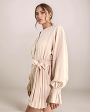 Woman wearing a beige dress with long sleeves against a plain background