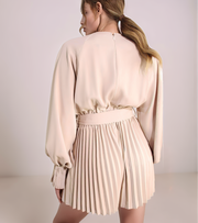 Woman wearing a beige blouse and pleated skirt against a plain background