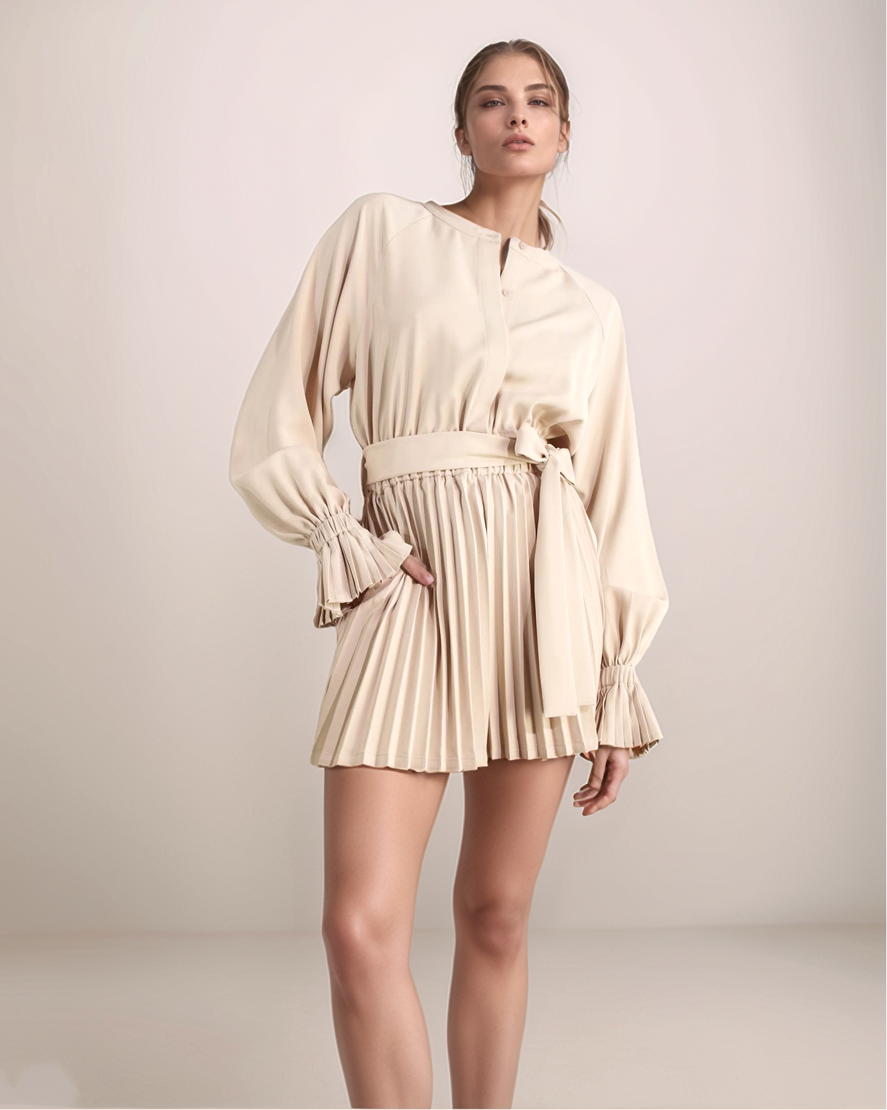 Woman wearing a cream-colored romper with long sleeves and pleated skirt on a plain background