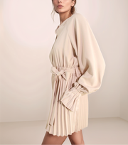 Woman wearing a beige dress with a belt against a plain background