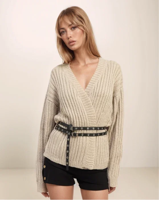Woman wearing a beige ribbed sweater with a belt against a plain background