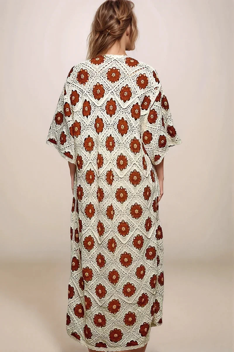 The back view of a long, openwork cream crochet cardigan with intricate floral patterns and 3/4 sleeves.