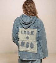 Person wearing a blue denim jacket with a patch on the back against a beige background