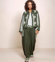 Woman wearing a green floral jacket and pants on a plain background