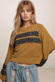Woman wearing a mustard yellow sweater with black floral details and blue jeans with floral patterns.