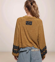 Person wearing a mustard yellow jacket with floral cuffs and back patch on a plain background