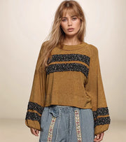 Woman wearing a brown sweater with black and white patterned sleeves against a beige background