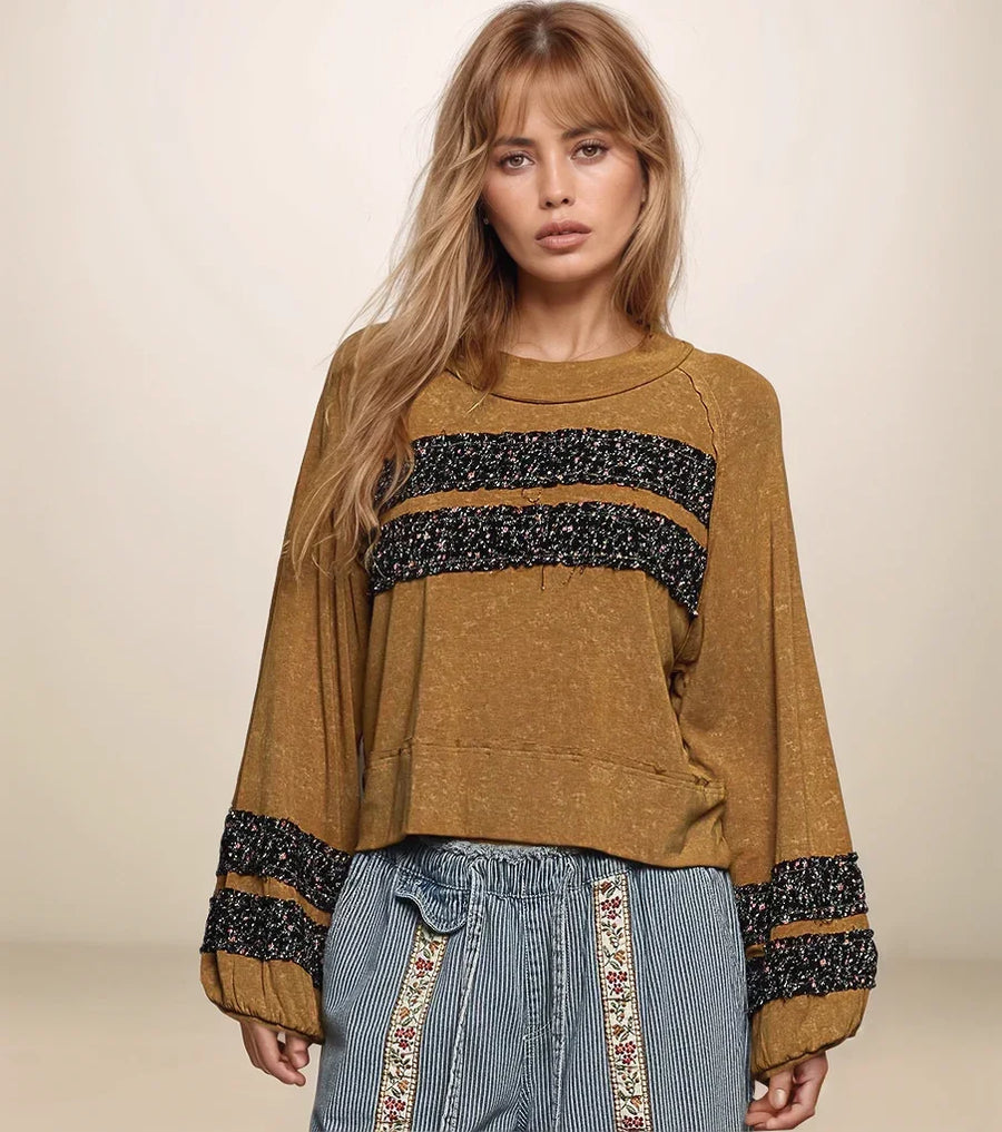 Woman wearing a brown sweater with black and white patterned sleeves against a beige background