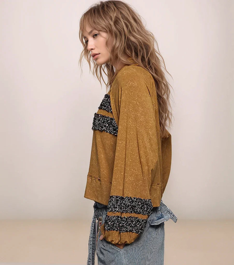 Woman wearing a mustard yellow cardigan with black and white patterned sleeves against a plain background