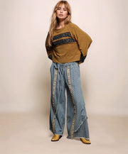 Woman wearing a brown sweater and blue jeans with decorative trim on a beige background