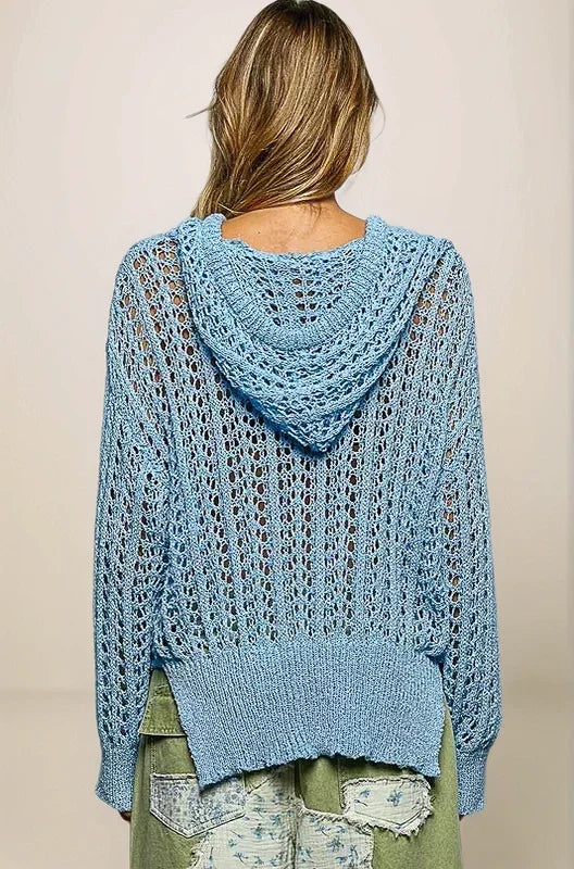 Back view of the light blue openwork sweater, showing the integrated hood resting on the shoulders and the intricate, airy texture across the back.