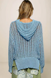 Back view of the light blue openwork sweater, showing the integrated hood resting on the shoulders and the intricate, airy texture across the back.