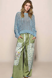 Full-body view of a model wearing the blue POL Skye sweater paired with olive green floral patch cargo pants, highlighting a relaxed and stylish transitional look.