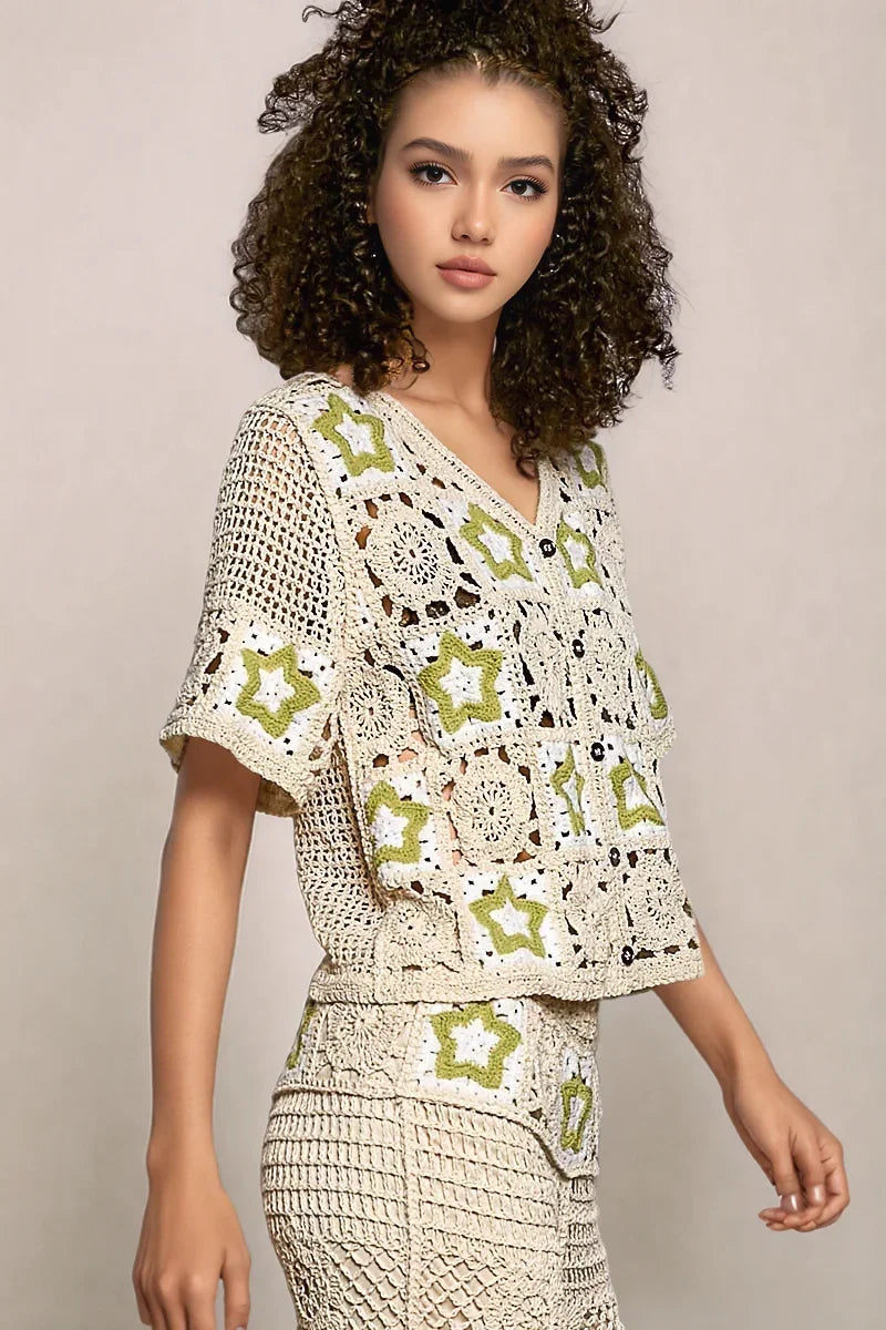 Angled front view of the short-sleeve Stardust cardigan, highlighting the airy, varied weave patterns and the playful green star motifs on the sleeves and bodice.
