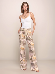 Woman wearing a white top and light pink camo pants against a plain background