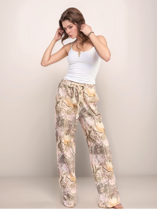 Woman wearing a white tank top and patterned pants against a plain background