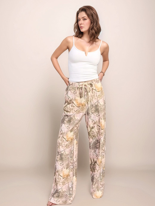 Woman wearing a white tank top and camopants against a plain background