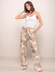 Woman wearing a white tank top and camo pants against a plain background