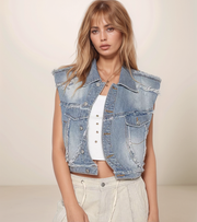 Woman wearing a denim vest over a white top with a neutral background