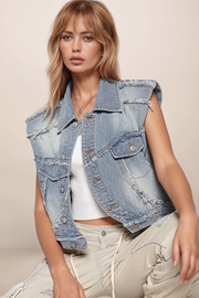 Woman wearing a denim vest over a white top and beige pants on a beige background