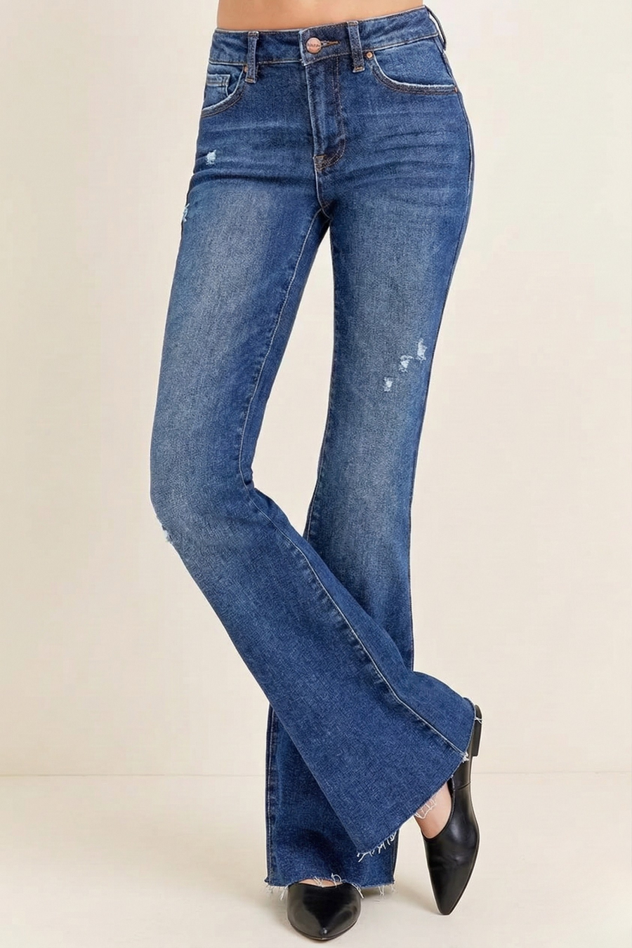 Blue vintage inspired jeans with light distressing and raw hem worn by a woman on a beige background