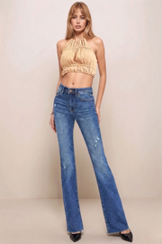 Woman wearing a tan top and blue jeans against a beige background