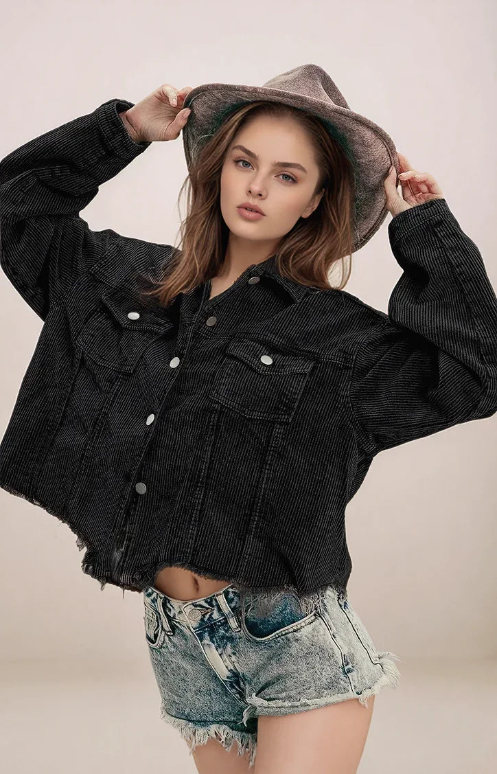 Woman wearing a black denim jacket and denim shorts with a hat on a plain background