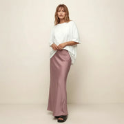 Woman wearing a white top and pink skirt against a beige background