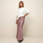 Woman wearing a white top and pink satin skirt against a beige background