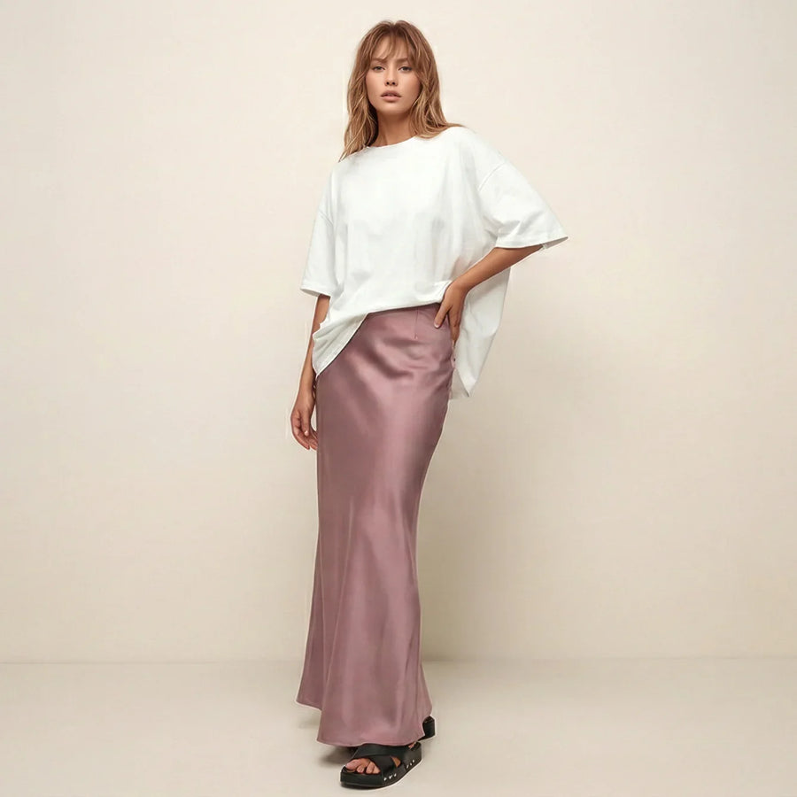 Woman wearing a white top and pink satin skirt against a beige background