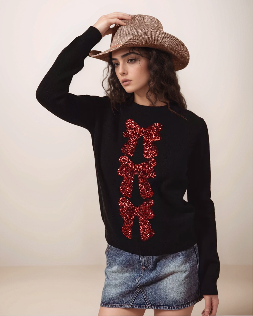 Woman wearing a black sweater with red sequin letters, denim skirt, and cowboy hat on a plain background