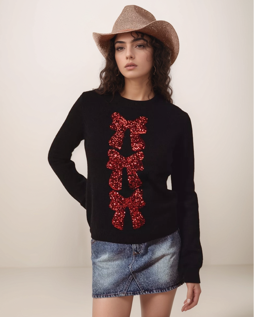 Woman wearing a black sweater with red sequin design, denim skirt, and cowboy hat on a plain background