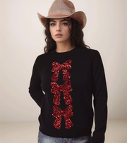 Woman wearing a black sweater with red sequin bows and a straw hat on a plain background