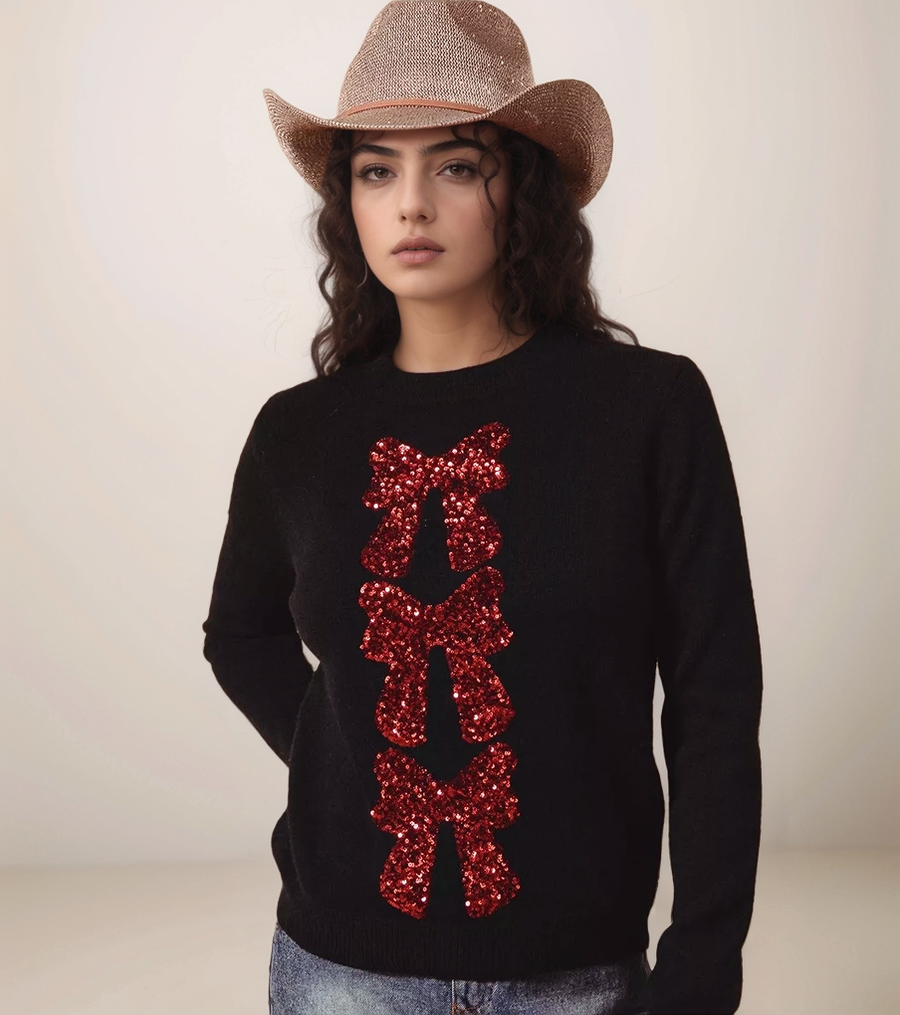 Woman wearing a black sweater with red sequin bows and a straw hat on a plain background