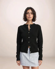 Woman wearing a black cardigan over a light blue skirt on a plain background