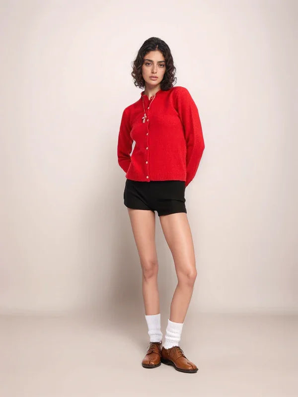 Woman wearing a red cardigan, black shorts, white socks, and brown shoes on a beige background