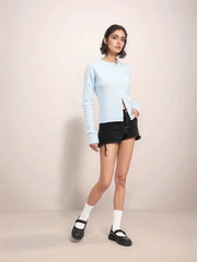 Woman wearing a light blue sweater and black shorts on a plain background