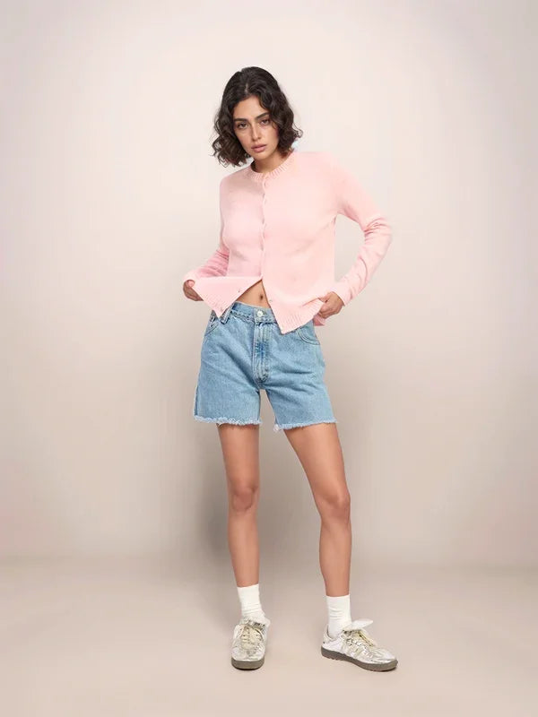 Woman wearing a pink cardigan, blue denim shorts, and white sneakers on a beige background