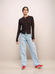 Woman wearing a black cardigan, light blue jeans, and red shoes on a beige background