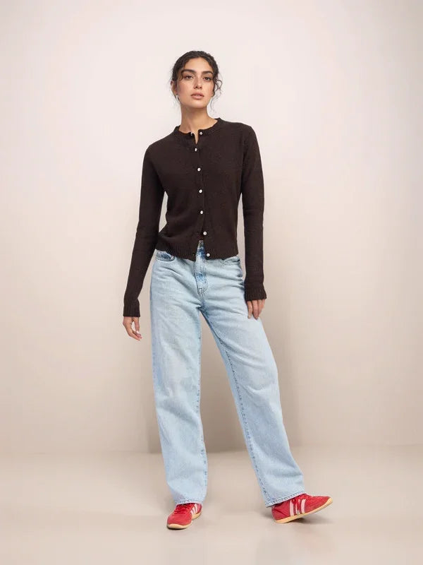 Woman wearing a black cardigan, light blue jeans, and red shoes on a beige background