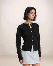 Woman wearing a black cardigan over a light blue top on a beige background