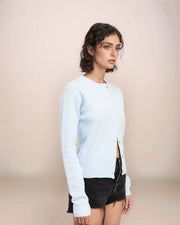 Woman wearing a light blue cardigan over a black top and shorts on a beige background