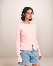 Person wearing a pink sweater and denim shorts on a plain background