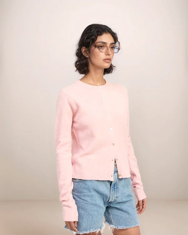 Person wearing a pink sweater and denim shorts on a plain background