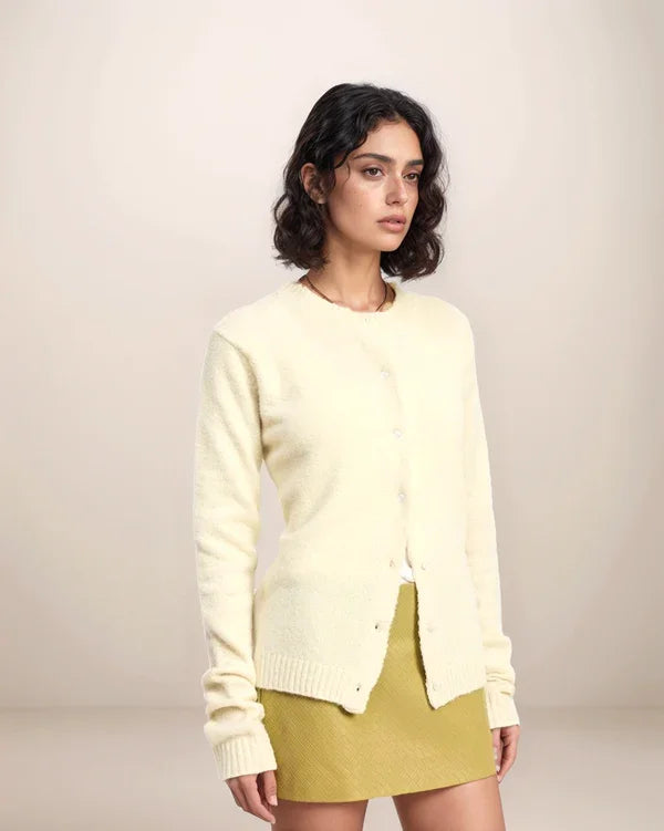 Woman wearing a light yellow sweater over a green skirt on a plain background