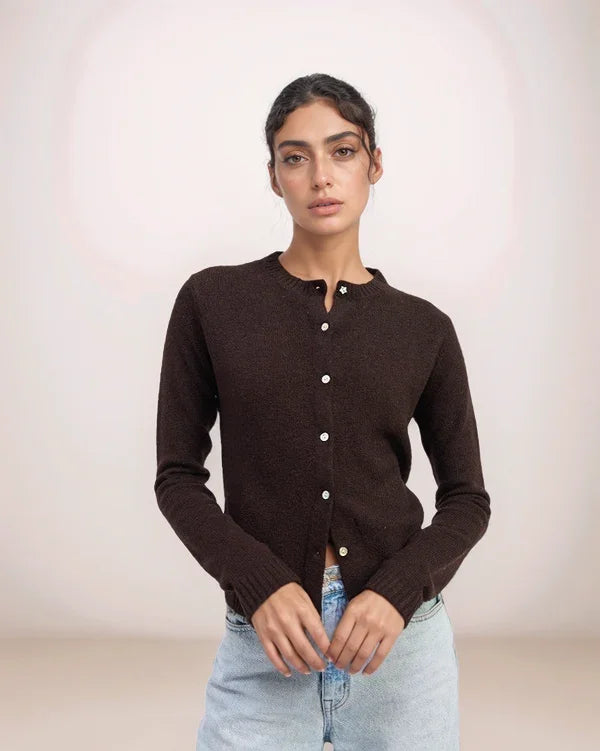 Woman wearing a brown cardigan with white buttons against a plain background
