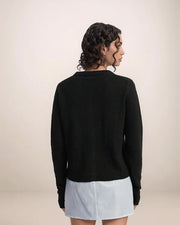 Person wearing a black sweater and light blue skirt on a beige background