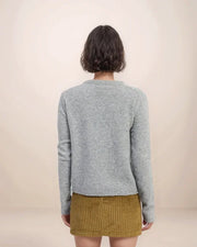Person wearing a gray sweater and mustard yellow skirt on a beige background