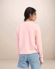 Person wearing a pink sweater and blue jeans against a beige background